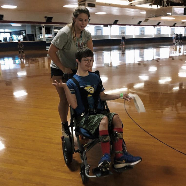 An ACAP assistant skating with an camper in a wheelchair.